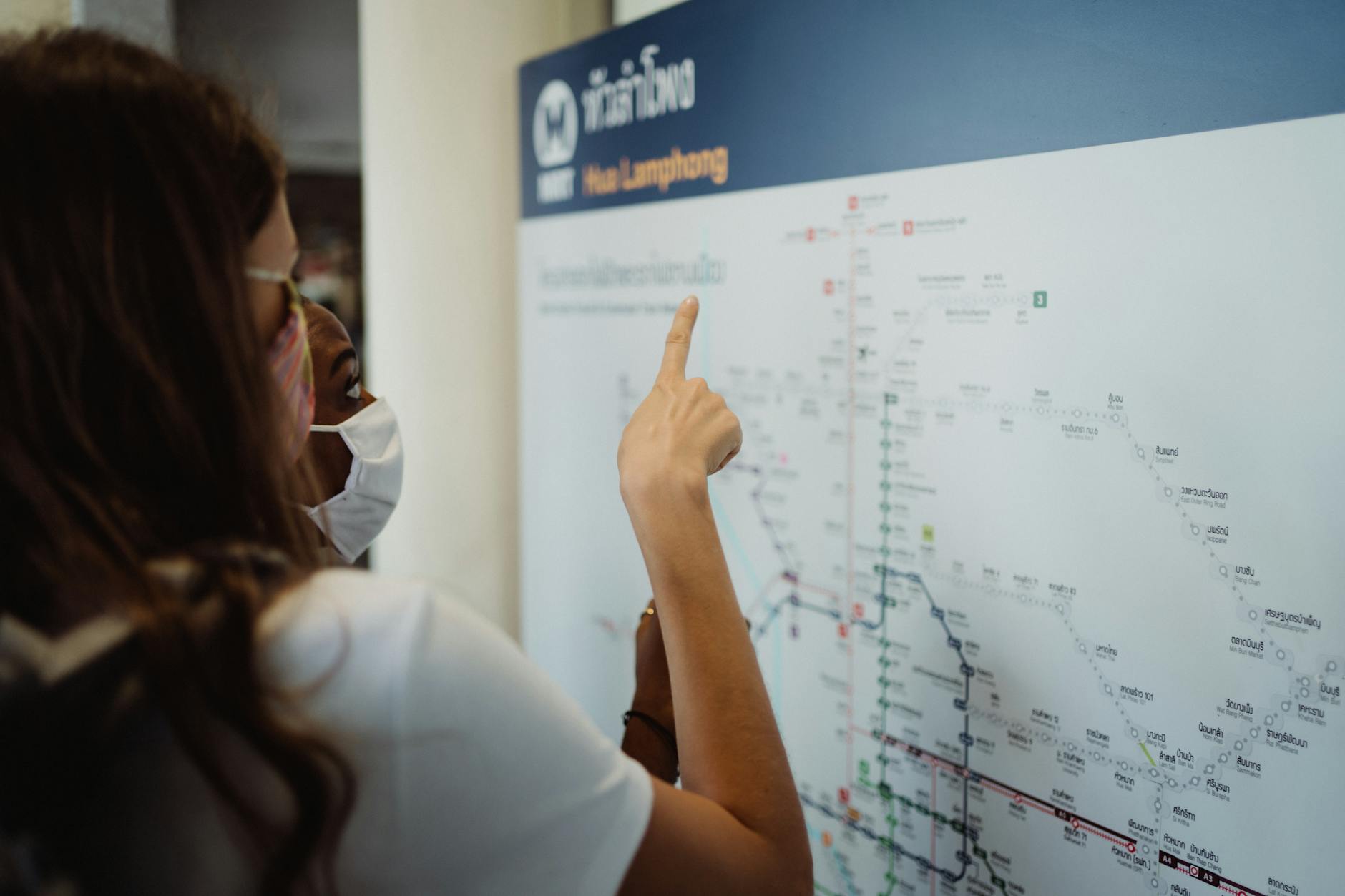 Dwie turystki w maseczkach analizują mapę transportu podczas podróży